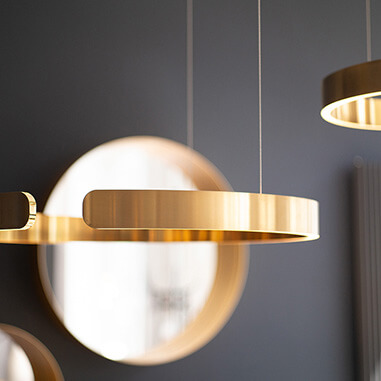 Goldene, moderne Pendelleuchten vor grauer Wand